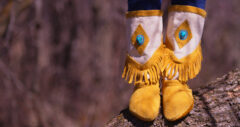 beaded and fringed mid-calf moccasins standing on log